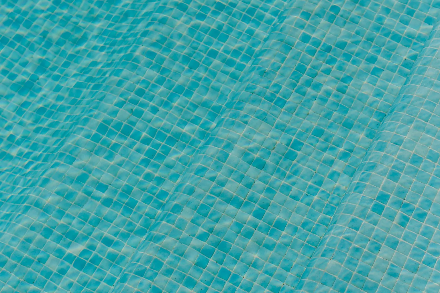 Close view of blue mosaic swimming pool floor tiles under clear rippling water
